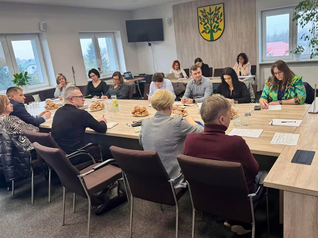 Oficjalne spotkanie w nowoczesnej sali konferencyjnej. Uczestnicy skupieni na dokumentach, atmosfera rzeczowa.