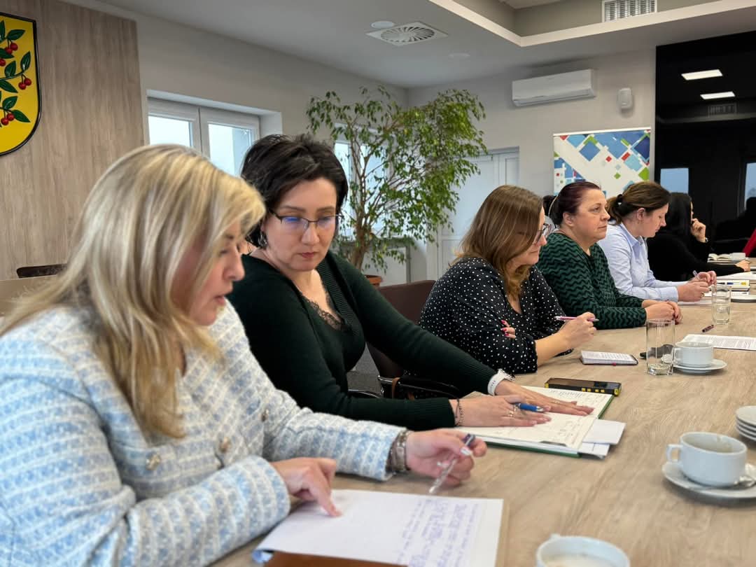 Oficjalne spotkanie w nowoczesnej sali konferencyjnej. Uczestnicy skupieni na dokumentach, atmosfera rzeczowa.